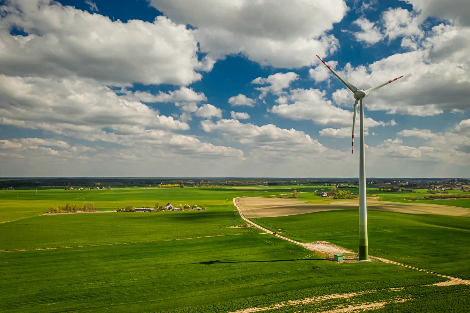 Wind turbine in green countryside under cloudy sky.